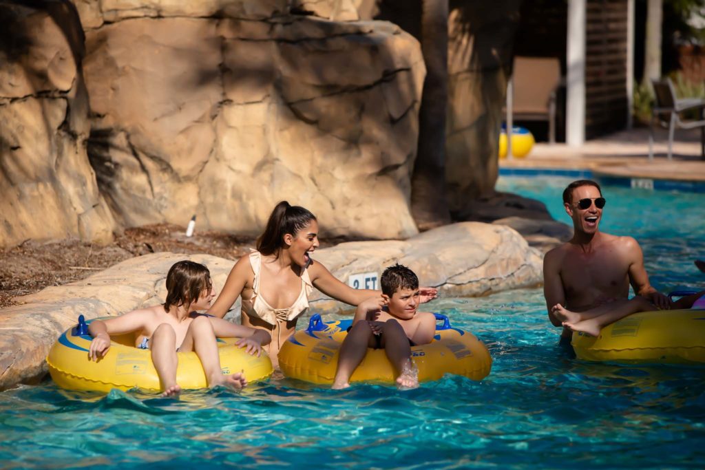 Kids Riding In Tube Floats As Their Parents Walk Through The Lazy River At The Spectrum Resort Orlando Water Park.