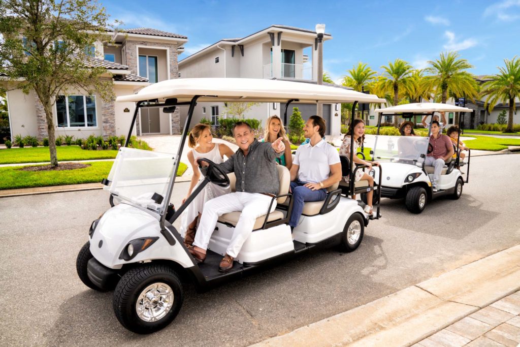 Familias que viajan en carros de golf frente a lujosas residencias turísticas e hileras de palmeras.