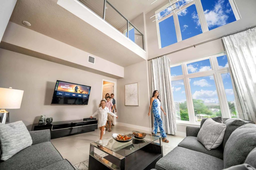 Familia de niños y padres corriendo hacia la sala de estar de una residencia de Spectrum Resort Orlando con una ventana grande.