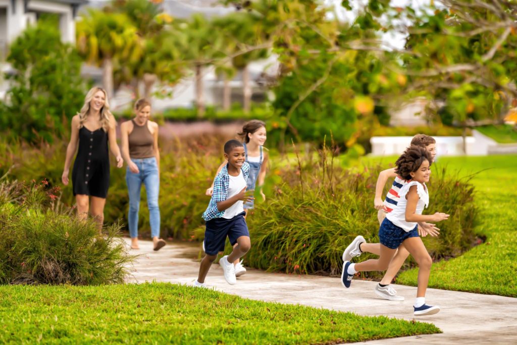 Niños corriendo fuera de su residencia de Spectrum Resort Orlando Resort mientras sus madres miran, sonriendo.