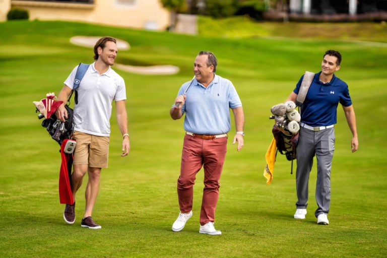 Grupo de tres hombres caminando con equipo de golf en los campos exclusivos de Spectrum Resort Orlando.