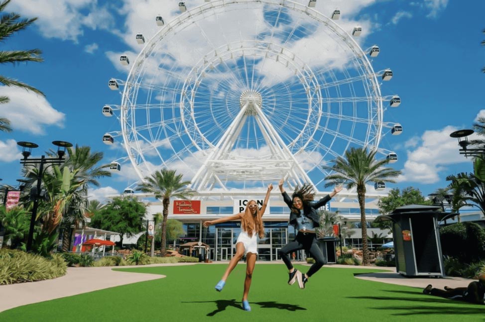 Two Women Jumping For Joy In Front Of The Icon Orlando Wheel, Also Known As The Orlando Eye.