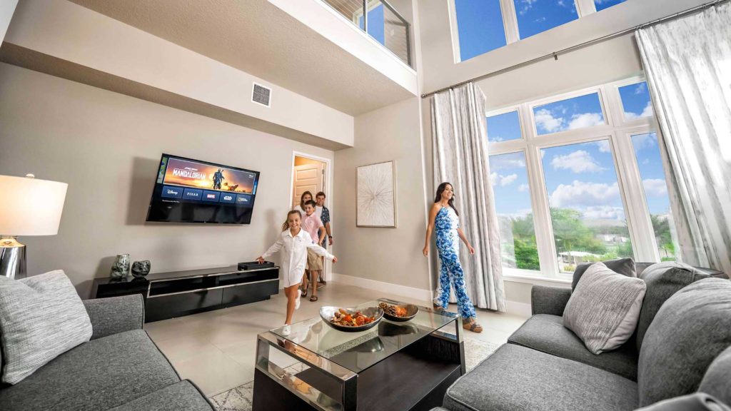 Family entering the spacious living room with floor-to-ceiling windows at their Spectrum Resort Orlando vacation home