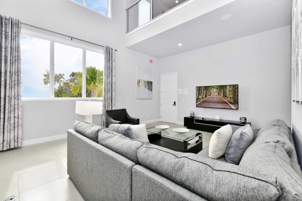 Sala de estar con sofá seccional, televisor montado en la pared y ventanales del piso al techo: Condominio de 4 habitaciones