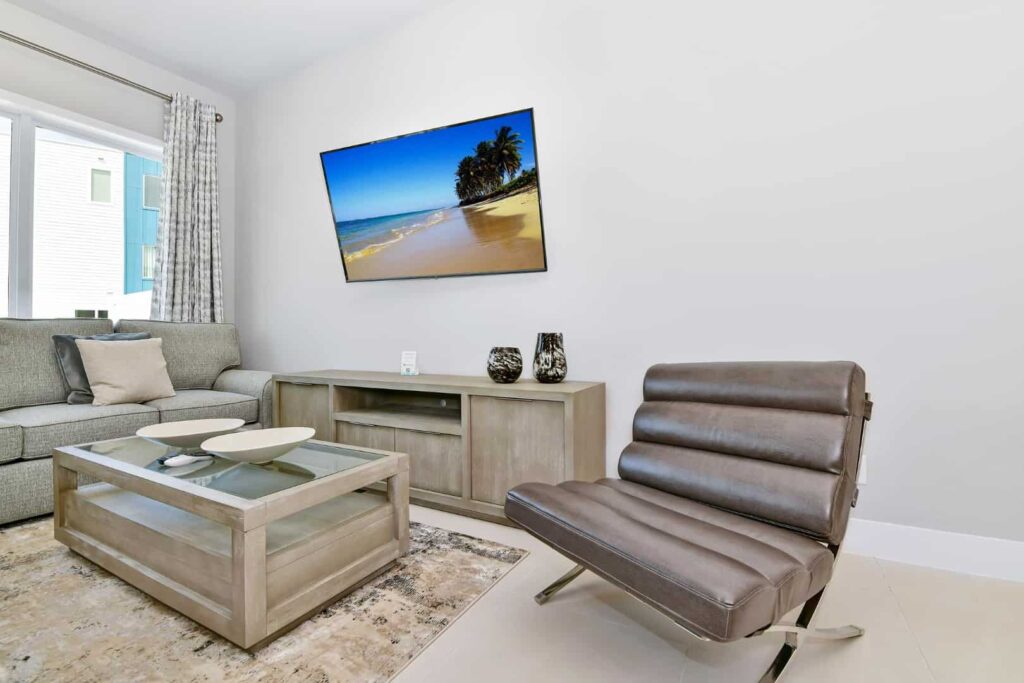 Sala de estar con sofá, silla decorativa, mesa de café y televisor montado en la pared