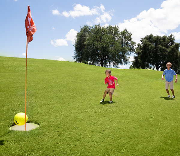 Metas de condición física: Niños jugando footgolf con una pelota de fútbol y hoyos de golf de gran tamaño