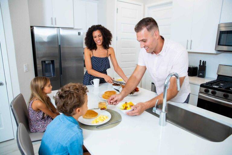 Parents serving breakfast to their kids sitting at the kitchen breakfast bar