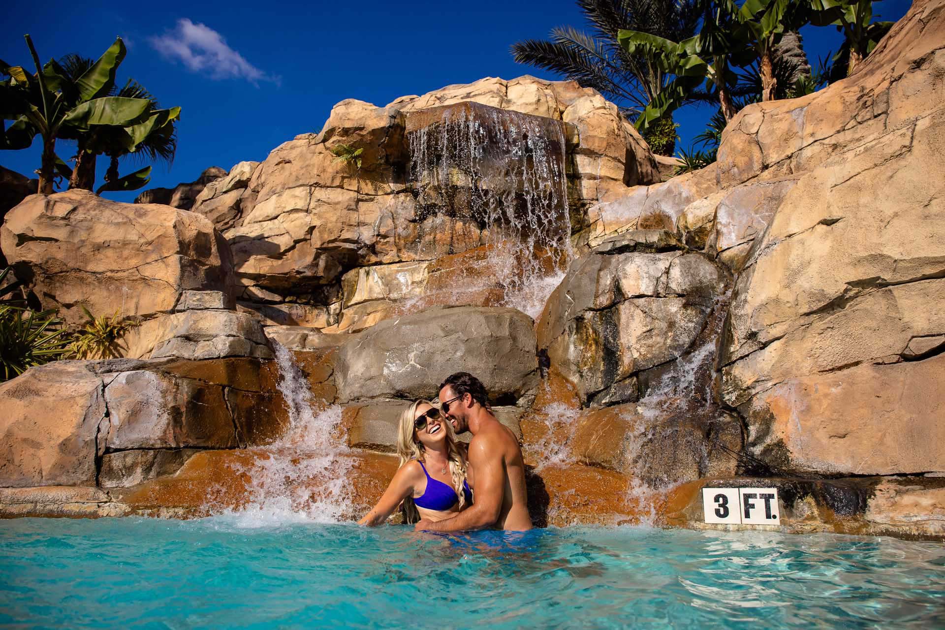 Couple enjoying time together in the pool next to a waterfall at the Reunion Resort Water Park