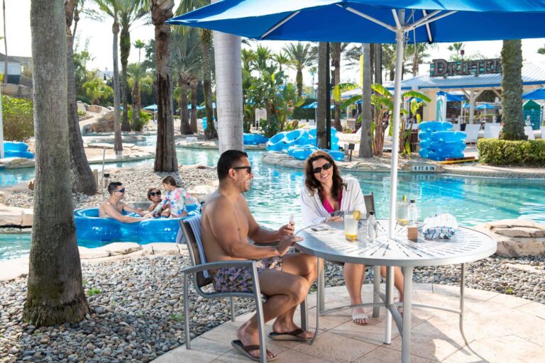 Couple playing a game of cards at a covered table next to the lazy river at the Reunion Resort Water Park