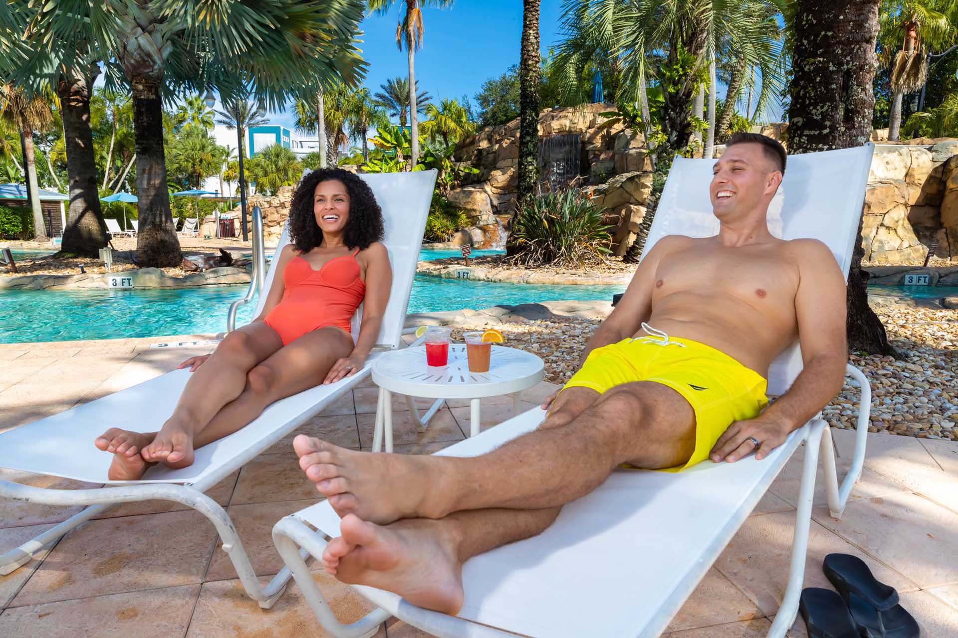 Couple relaxing with cocktails in lounge chairs by a pool at the Reunion Resort Water Park