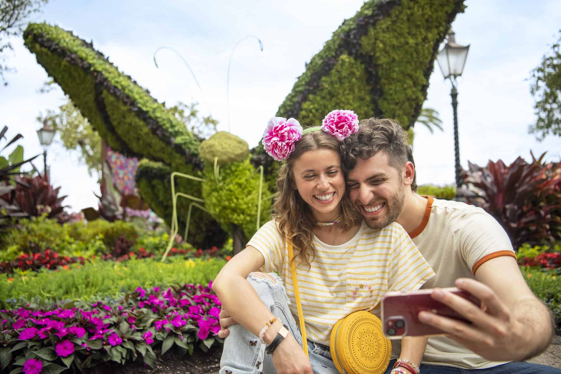 Pareja posando para una foto selfie frente a un topiario de mariposas en el Epcot Flower and Garden Festival de Disney