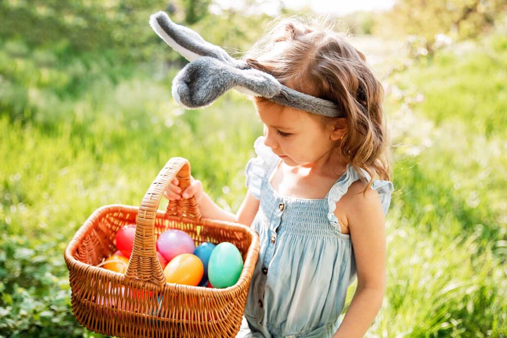 Young girl wearing bunny ears, holding a basket of Easter eggs