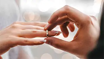 Weddings: Groom’s hand placing a wedding ring on bride’s hand